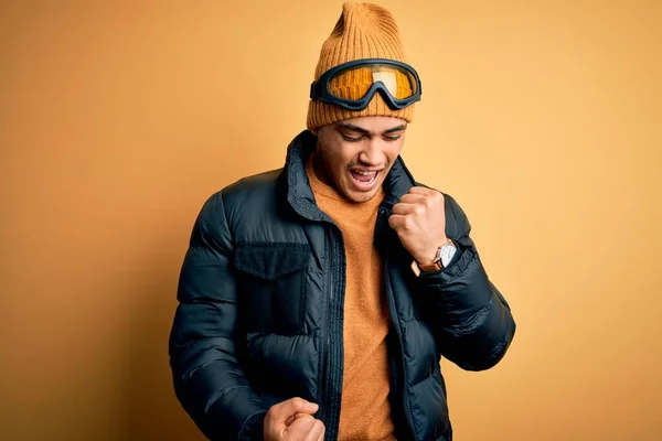 年轻的巴西滑雪者 身穿雪地运动服 戴着黄种人背景的滑雪护目镜 高举双臂 闭上眼睛 为成功感到惊奇和惊奇 赢的概念 — 图库照片
