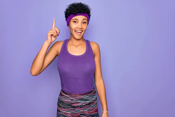 Beautiful african american afro woman wearing casual sportswear over purple background pointing finger up with successful idea. Exited and happy. Number one.