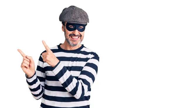 中年ハンサムな男を身に着けています泥棒マスク笑顔とカメラを見てポインティングで二本の手と指で側面 — ストック写真