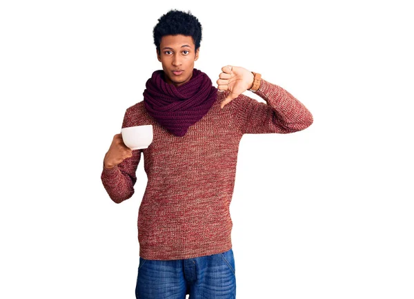若いアフリカ系アメリカ人の男性は 冬のスカーフを着て 怒りの顔をした熱いコーヒーを飲んで 親指で嫌いを示す負の記号 拒否の概念 — ストック写真