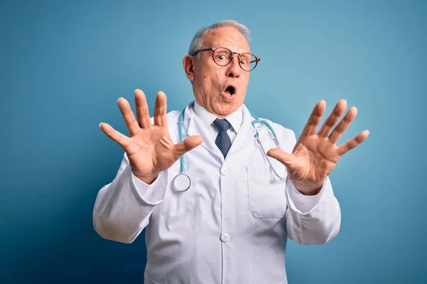 Starszy Siwy Lekarz Noszący Stetoskop Płaszcz Medyczny Niebieskim Tle Przestraszony — Zdjęcie stockowe
