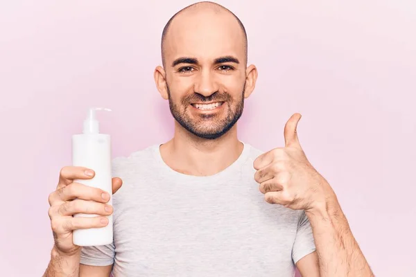 Joven Hombre Calvo Guapo Sosteniendo Botella Crema Loción Sonriendo Feliz — Foto de Stock