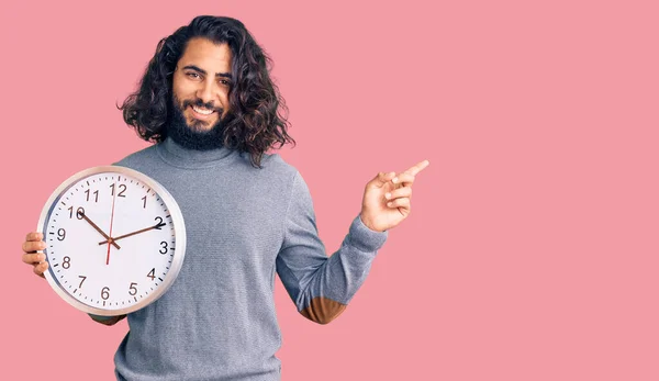 Młody Arabski Człowiek Trzyma Duży Zegar Uśmiechając Szczęśliwy Wskazując Ręką — Zdjęcie stockowe