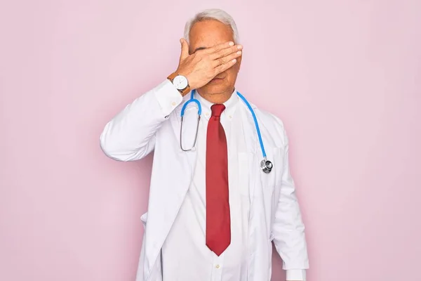 中世のシニア白髪の医者の男は手で目をカバー聴診器とプロの医療コートを身に着けています 深刻と悲しい見て 見えない 隠れている 拒絶の概念 — ストック写真