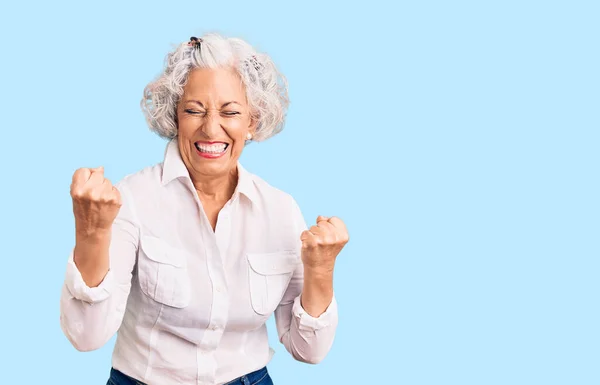 头发灰白的老年妇女穿着休闲装 非常快乐而兴奋地做着获胜的手势 举起双臂 微笑着 尖叫着要成功 庆祝概念 — 图库照片