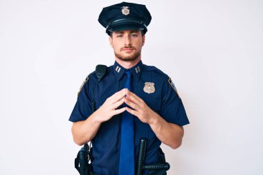 Polis üniforması giyen genç beyaz adam ellerini birleştirip gülümseyerek gevşemiş ve neşeliydi. Başarı ve iyimserlik 