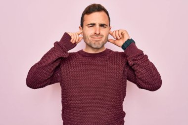 Mavi gözlü genç adam pembe arka planda dikilip yüksek sesli müzik sesi için kulaklarını parmaklarıyla kapatıyor. Sağır kavramı.