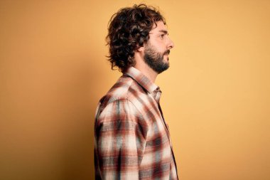 Sakallı, sıradan tişörtlü, sarı arka planda dikilmiş, rahat bir görünüm takınan, kendine güvenen gülümseyen genç yakışıklı bir adam..