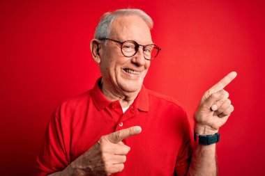 Gri saçlı, gözlüklü ve kırmızı arka planda rahat tişörtlü bir adam gülümsüyor ve kameraya bakıyor..