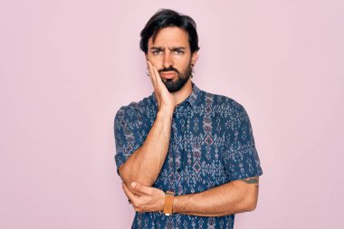 Pembe arka planda hippi tarzı giyinen yakışıklı İspanyol bohem adam kollarını kavuşturup depresyondan sıkılmış ve yorgun görünüyor..