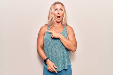 Orta yaşlı, beyaz giysili, sarışın bir kadın. Yan tarafı işaret ederek şaşırmış, ağzı açık, şaşkın bir ifade.. 