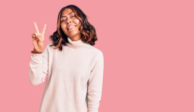 Kış balıkçı yaka kazak giyen genç ve güzel bir ırk kadını parmaklarıyla iki numarayı gösterirken kendinden emin ve mutlu bir şekilde gülümsüyor.. 