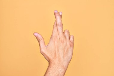 Kafkas genci parmaklarını izole edilmiş sarı arka plan üzerinde gösteriyor. Parmaklarını çapraz yapıyor, batıl inançlar ve şanslı bir jest, şanslı ve umut dolu bir ifade.