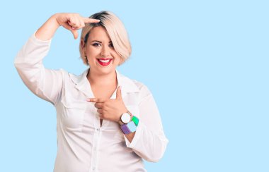 Genç sarışın, iri yarı, rahat tişört giyen, gülümseyen, elleri ve parmakları mutlu yüzlü bir kadın. yaratıcılık ve fotoğrafçılık kavramı. 