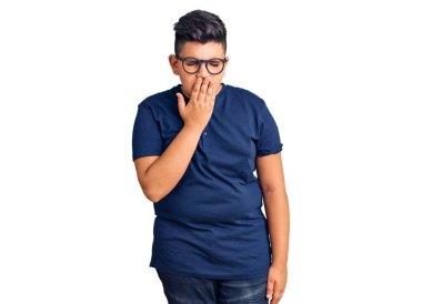 Günlük kıyafetler ve gözlük takan küçük çocuk ağzıyla ağzını kapatmaktan sıkılmış. Huzursuz ve uykulu.. 