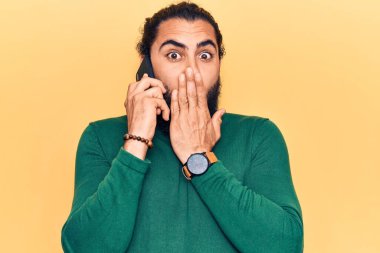 Genç Arap adam akıllı telefondan konuşuyor. Ağzını eliyle kapatıyor. Şok geçiriyor ve hata yapmaktan korkuyor. şaşırmış ifade 