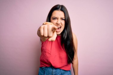 Genç esmer kadın pembe izole edilmiş arka plan üzerine gündelik bir tişört giyiyor. Kameraya kızgın ve sinirli olduğunu gösteriyor.