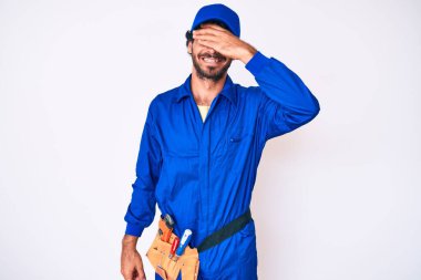 Kıvırcık saçlı yakışıklı genç adam ve ayı gibi giyinen tamirci üniforması. Gülümseyen ve gülen elleri yüzüyle şaşırtmak için gözleri kapatan adam. kör kavram. 