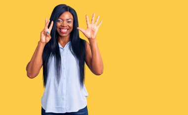 Genç Afro-Amerikalı kadın günlük giysiler giyiyor ve 8 numaralı parmaklarıyla işaret ederken kendinden emin ve mutlu gülümsüyor.. 