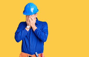 Genç yakışıklı adam işçi üniforması giyiyor ve kafasında el olan bir şapka var. Stres yüzünden başı ağrıyor. migren ağrısı. 