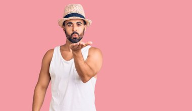 Gündelik yaz şapkası takan genç İspanyol adam kameraya bakıp havada el sallayarak öpüşüyor ve sevimli ve seksi oluyor. aşk ifadesi. 