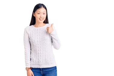 Genç, güzel, Çinli bir kadın, sıradan bir kazak giyip mutlu mesut el hareketi yapıyor. Kameraya bakıp başarıyı gösteren ifade. 