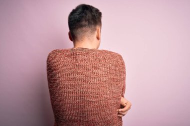 Pembe soyutlanmış arka plan üzerine sıradan bir kazak giyen yakışıklı beyaz bir adam mutlu ve pozitif bir şekilde sarılıyor. Sevgi ve özgüven.