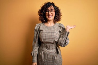 Güzel bir Arap iş kadını. Elbise ve gözlük takıyor. Sarı arka planda duruyor..