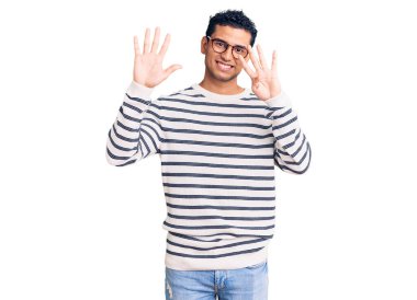 İspanyol asıllı yakışıklı genç adam gündelik kıyafetler giyiyor ve gözlük takıyor dokuz numaralı parmaklarıyla işaret ediyor ve gülümsüyor kendinden emin ve mutlu.. 