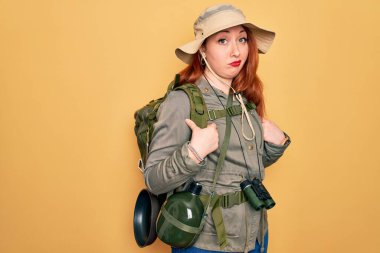 Sırt çantalı, sarı arka plan kuşkucu ve sinirli genç, sırt çantalı, sırt çantalı ve şapkalı, sorun yüzünden kaşlarını çatan kızıl saçlı kadın. Negatif kişi.