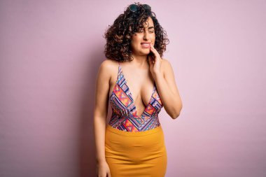 Genç, güzel bir Arap kadın, diş ağrısı ya da diş ağrısı yüzünden pembe arka planda güneş gözlüğü takıp ağza dokunuyor. Dişçi