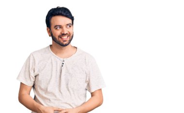 Gündelik kıyafetler giyen genç İspanyol bir adam yüzünde gülümsemeyle yan yana bakıyor, doğal bir ifade. Kendinden emin gülen. 