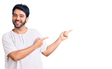 Gündelik kıyafetler giyen genç İspanyol adam gülümseyip kameraya bakıyor ve iki eliyle ve parmaklarıyla kenarı işaret ediyor.. 