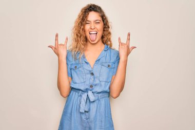 Mavi gözlü genç bir kadın beyaz arka plan üzerine günlük kot elbise giymiş çılgın bir ifadeyle elleri havada rock sembolü yaparak bağırıyor. Müzik yıldızı. Ağır konsept.