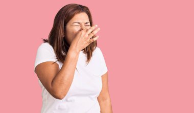 Orta yaşlı, beyaz tişört giyen Latin bir kadın pis ve iğrenç bir koku alıyor. Nefesini burnunda tutuyor. Kötü kokuyor. 