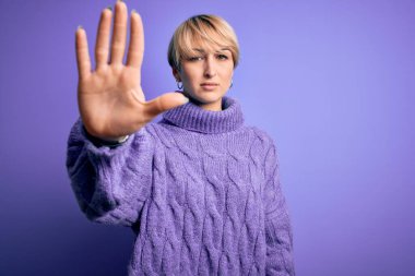 Kısa saçlı, mor arka planda balıkçı yaka kazak giyen genç sarışın kadın avucunun içi gibi şarkı söylemeyi kesiyor. Yüzünde olumsuz ve ciddi bir jest olan uyarı ifadesi.