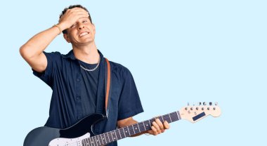 Elektro gitar çalan genç yakışıklı adam gergin ve hayal kırıklığına uğramış, şaşırmış ve kızgın yüzlü. 