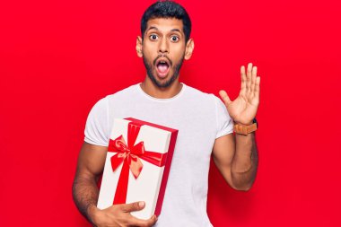 Genç latin adam hediyesini tutuyor. Korkmuş ve ağzı açık kalmış, şaşırmış ve şaşırmış. 