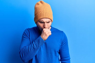 Gündelik kazak giyen ve yün şapka takan genç yakışıklı adam kendini iyi hissetmiyor ve soğuk algınlığı veya bronşitin belirtisi olarak öksürüyor. sağlık hizmeti kavramı. 