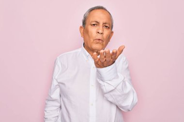 Üst düzey yakışıklı, gri saçlı, zarif tişörtlü, pembe arka planda, kameraya bakıp havada öpücükler saçan, güzel ve seksi bir adam. Aşk ifadesi.