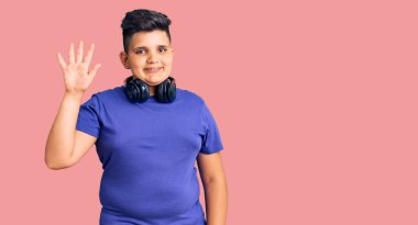 Küçük çocuk müzik dinliyor kulaklık takıyor ve beş numaralı parmaklarıyla işaret ediyor kendinden emin ve mutlu gülümsüyor.. 