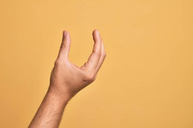 İzole edilmiş sarı arka plan üzerinde parmaklarını gösteren beyaz bir adamın eli. Görünmez bir şeyi alıp, parmaklarıyla uzayı gösteren bir nesneyi tutuyor.