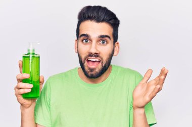 Sakallı genç yakışıklı adam bir şişe aloe vera kremi giyerek başarıyı mutlu bir gülümsemeyle ve kazanan yüz ifadesini kaldırarak kutluyor. 