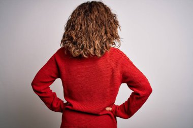 Orta yaşlı esmer kadın, sıradan bir süveter giyiyor izole edilmiş beyaz arka planda dikiliyor geriye bakıyor kolları vücudunda.
