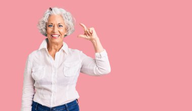 Yaşlı, gri saçlı, günlük kıyafetler giyen, gülümseyen, kendine güvenen, el hareketleriyle küçük beden işareti yapan, parmaklarını gösterip kameraya bakan bir kadın. ölçüm kavramı. 