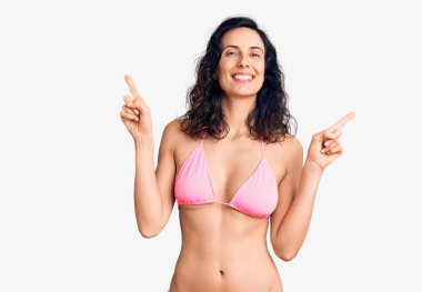 Bikini giyen, kendine güvenen, parmaklarıyla farklı yönleri gösteren genç ve güzel bir İspanyol kadın. reklam için kopyalama alanı 