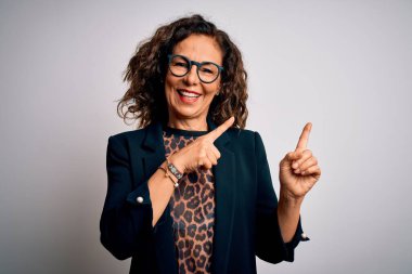 Orta yaşlı esmer iş kadını gözlüklü, izole edilmiş beyaz arka planda duran, gülümseyen ve kameraya bakan iki eli ve parmakları yandan gösteren..