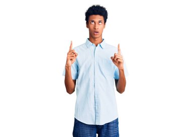 Gündelik giysiler giyen genç Afro-Amerikan adam şaşkın ve şaşırmış bir şekilde yukarı baktı ve parmaklarıyla işaret etti ve kollarını kaldırdı.. 