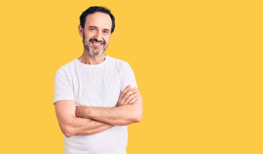 Orta yaşlı yakışıklı, sıradan tişörtlü, mutlu yüzlü, kollarını kavuşturup kameraya bakan bir adam. pozitif kişi. 