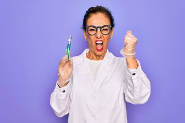 Laboratuvar önlüğü giyen orta yaşlı bir bilim kadını elinde test tüpü tutarken sinirlenmiş ve sinirlenmiş bir şekilde bağırıyor.